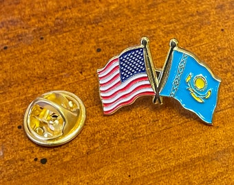 Puede incluir: Un pin de solapa de metal dorado con dos banderas cruzadas: la bandera de los Estados Unidos con franjas y estrellas rojas, blancas y azules, y la bandera azul claro de Kazajistán con un sol y un águila amarillos. Incluye un cierre metálico.