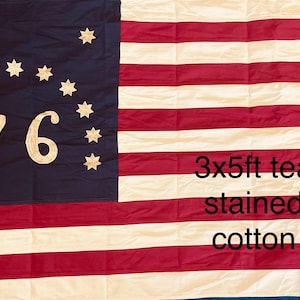 May include: A white ceramic mug with a black handle and the text "But First, Coffee" in a bold, black font. The mug is set against a blurred background, suggesting a cozy setting.