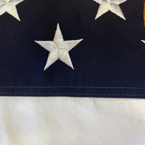 K&ouml;nnte beinhalten: Nahaufnahme einer blau-wei&szlig;en amerikanischen Flagge mit wei&szlig;en Sternen, die auf das blaue Feld gen&auml;ht sind. Die Flagge ist in drei Teile gefaltet, wobei die wei&szlig;en Streifen unten sichtbar sind.
