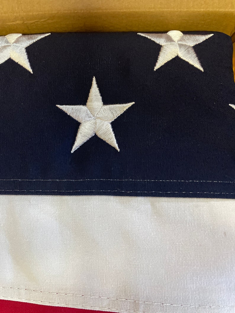 K&ouml;nnte beinhalten: Nahaufnahme einer blau-wei&szlig;en amerikanischen Flagge mit wei&szlig;en Sternen, die auf das blaue Feld gen&auml;ht sind. Die Flagge ist in drei Teile gefaltet, wobei die wei&szlig;en Streifen unten sichtbar sind.