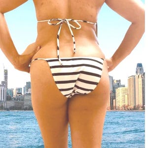 May include: A person wearing a black and white striped bikini standing in front of a body of water with a city skyline in the background.