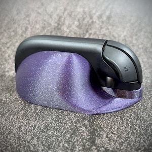 Peut inclure: Un accessoire de manette de jeu noir et violet. L'accessoire a une base incurvée violette et scintillante et une section supérieure noire avec un bouton étiqueté "ZR". L'article est conçu pour contenir une manette de jeu.