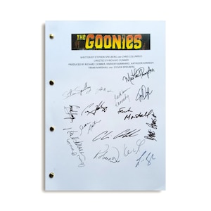 Op de afbeelding: Een wit vel papier met de titel "The Goonies" in zwarte en rode letters. Het papier is gesigneerd door verschillende mensen, waaronder Steven Spielberg, Kathleen Kennedy en Frank Marshall.