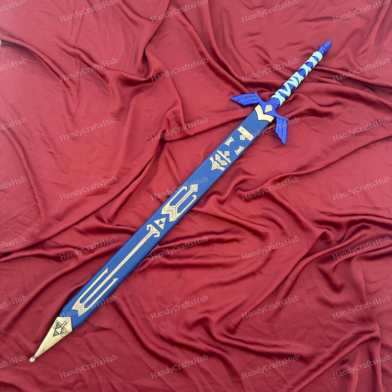 Puede incluir: Una espada decorativa azul y dorada con un dise&ntilde;o estilizado. La espada presenta una punta de hoja dorada, un mango azul con un patr&oacute;n azul claro y blanco, y adornos dorados a lo largo de la hoja. La espada mide aproximadamente 102 cm de largo.