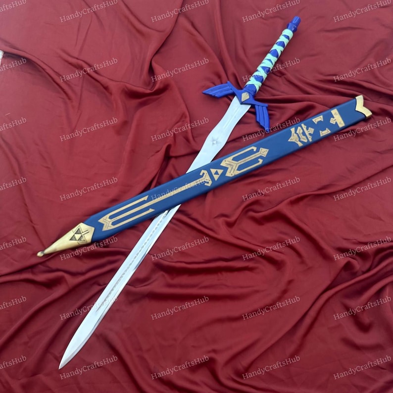 Puede incluir: Imagen detallada de una espada y vaina de fantas&iacute;a. La espada presenta una hoja plateada, guarda azul y empu&ntilde;adura azul claro y blanca. La vaina es azul con detalles dorados y una punta dorada. Los art&iacute;culos se muestran sobre una superficie burdeos.