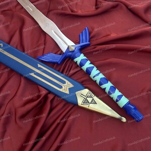 Puede incluir: Espada de fantas&iacute;a azul y plateada con vaina a juego. La espada presenta una hoja plateada, una empu&ntilde;adura azul con un acento en forma de diamante y un mango envuelto en azul y azul claro. La vaina es azul con detalles dorados.