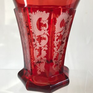 May include: A red glass goblet with a white etched design. The goblet has a hexagonal base and a flared rim.