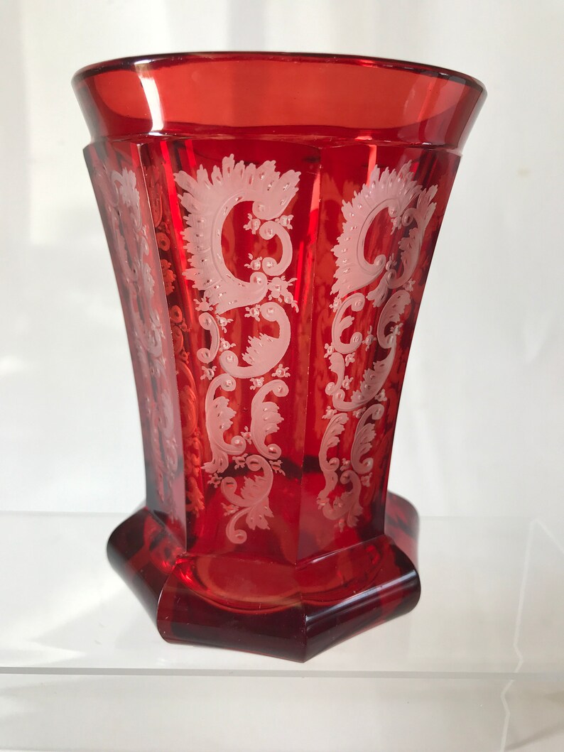 May include: A red glass goblet with a white etched design. The goblet has a hexagonal base and a flared rim.