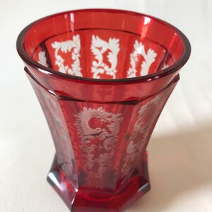 May include: A red glass goblet with a white etched design. The goblet has a wide mouth and a rounded base.
