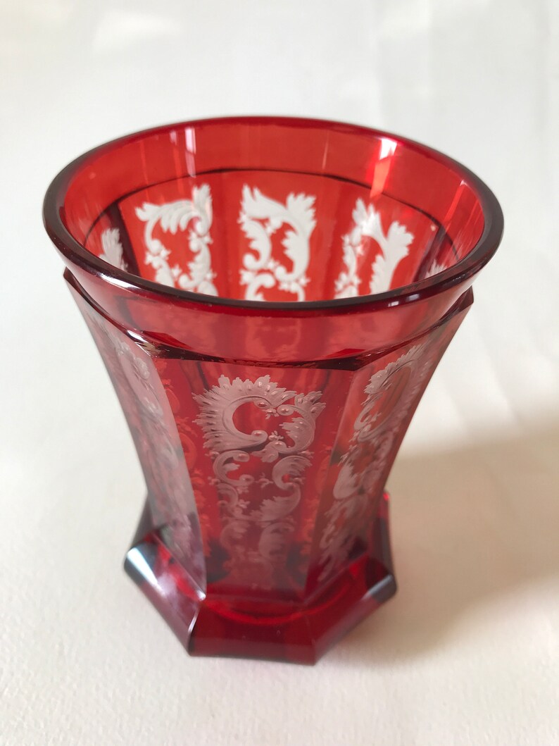 May include: A red glass goblet with a white etched design. The goblet has a wide mouth and a rounded base.