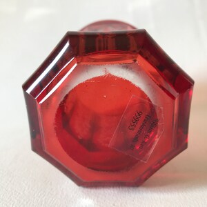 May include: Red glass vase with an octagonal base. The bottom of the vase has a label that reads "William C. Kraus Frankenmuth, MI 99653".