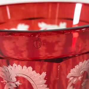 May include: A red glass goblet with a white etched design. The goblet has a rounded base and a flared rim.