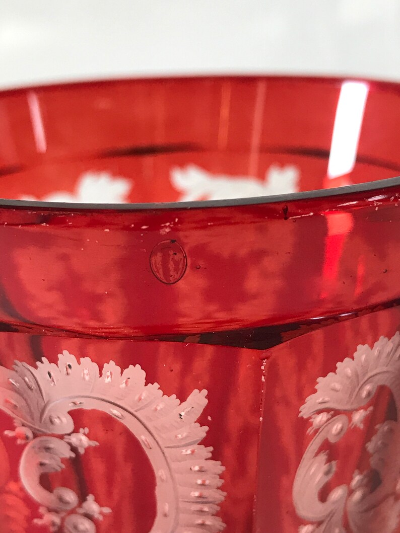 May include: A red glass goblet with a white etched design. The goblet has a rounded base and a flared rim.
