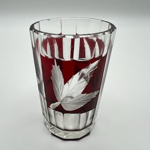 Op de afbeelding: Een helder glazen tumbler met een facetontwerp en een dieprode binnenkant. Het glas heeft een mat bladontwerp. De tumbler is ongeveer 10 cm hoog.