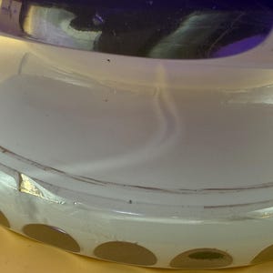 Op de afbeelding: Close-up van een decoratief glazen object met een witte basis en een donkerblauwe bovenkant. De basis heeft een reeks bruine cirkelvormige accenten. Het object lijkt een vaas of decoratieve kom te zijn.