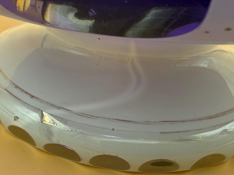 Op de afbeelding: Close-up van een decoratief glazen object met een witte basis en een donkerblauwe bovenkant. De basis heeft een reeks bruine cirkelvormige accenten. Het object lijkt een vaas of decoratieve kom te zijn.