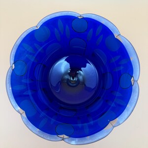Op de afbeelding: Een levendige blauwe glazen kom met een geschulpte rand. De kom heeft een bloemmotief met donkerblauwe cirkels en bladvormen. De rand is een lichtere tint blauw, wat een contrasterende rand cre&euml;ert. De binnenkant van de kom reflecteert het licht.