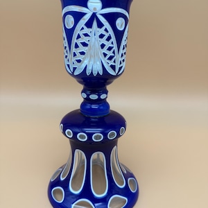 May include: A cobalt blue cut-to-clear glass goblet featuring intricate geometric patterns, including a lattice design on the upper bowl and circular motifs on the base. The glass transitions from deep blue to clear where the surface is cut away.