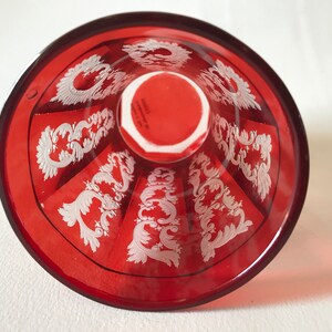 May include: The bottom of a red glass goblet with a white etched design. The design features a repeating pattern of stylized floral motifs.