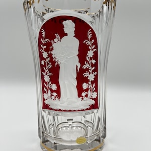 May include: A clear glass vase with a red and white cameo design. The vase has a gold rim and a gold band around the bottom. The cameo design features a woman holding a bouquet of flowers.