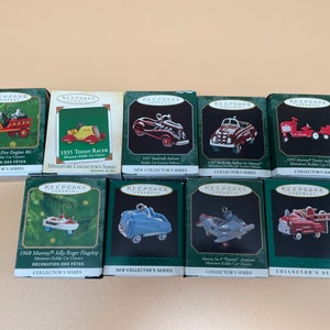 Könnte beinhalten: Eine Sammlung von Hallmark Keepsake-Ornamenten mit Miniatur-Oldtimern und Flugzeugen. Die Ornamente befinden sich in ihren Originalverpackungen mit grünen und weißen Verpackungen. Die Sammlung umfasst Feuerwehrautos, Rennwagen und Flugzeuge.