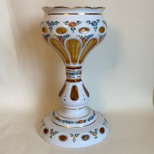 Op de afbeelding: Een sierlijke witte vaas met een geschulpte rand en een ronde basis. Het heeft gouden accenten en is versierd met kleurrijke bloemmotieven. De vaas is ongeveer 30 cm hoog.