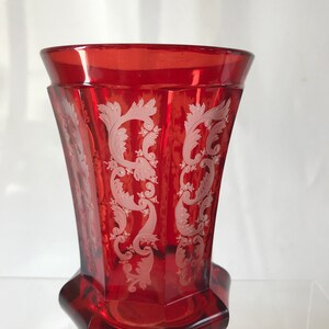 May include: A red glass vase with a white etched design. The vase has a flared top and a hexagonal base.