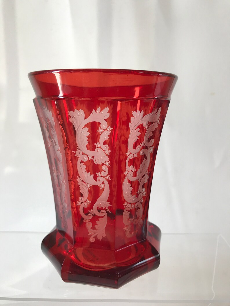 May include: A red glass vase with a white etched design. The vase has a flared top and a hexagonal base.