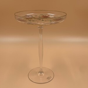 Op de afbeelding: Een hoge, transparante glazen voetkom met een gouden rand en een bloemenmotief. De kom heeft een delicate steel en een brede voet.
