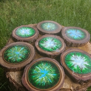 May include: Six round wooden coasters with a green and blue epoxy resin design. The design features a circular pattern of trees with a blue sky in the center.