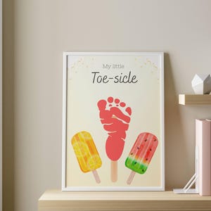 May include: A framed print featuring the text "My little Toe-sicle" above a red footprint and three watercolor popsicle illustrations. The popsicles are yellow with lemon slices, red, and green with watermelon slices.