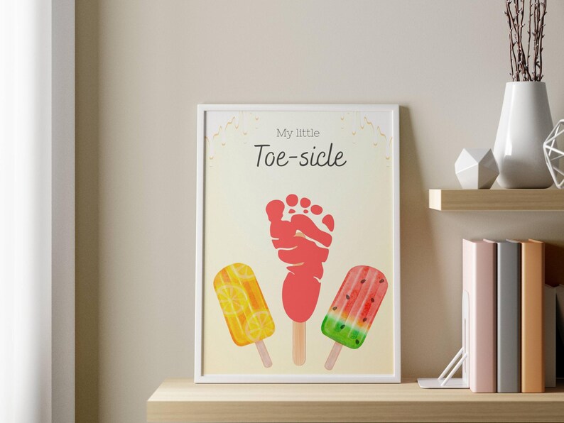 May include: A framed print featuring the text "My little Toe-sicle" above a red footprint and three watercolor popsicle illustrations. The popsicles are yellow with lemon slices, red, and green with watermelon slices.