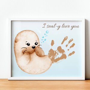 Può includere: Stampa incorniciata con un disegno di foca e un'impronta della mano, con la scritta "I seal-y love you". La foca è marrone chiaro, l'impronta della mano è marrone scuro. Sono presenti anche bolle blu.