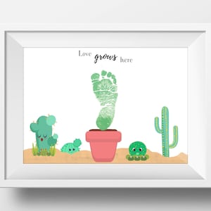 May include: A white framed print with the text "Love grows here" and a green footprint in a pink pot surrounded by three green cactus plants.