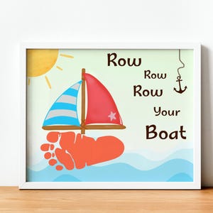 May include: A framed print featuring a whimsical illustration of a sailboat with a red sail and a blue and white striped sail. The boat is made from a footprint. The words "Row, Row, Row Your Boat" are written on the print.
