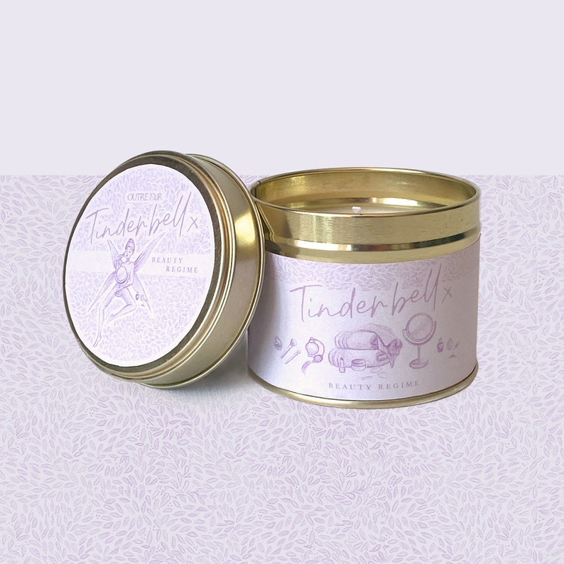 May include: A gold tin candle with a pink and white label that says "OUTRE PAR TINDERBELLx BEAUTY REGIME". The label features a fairy illustration.