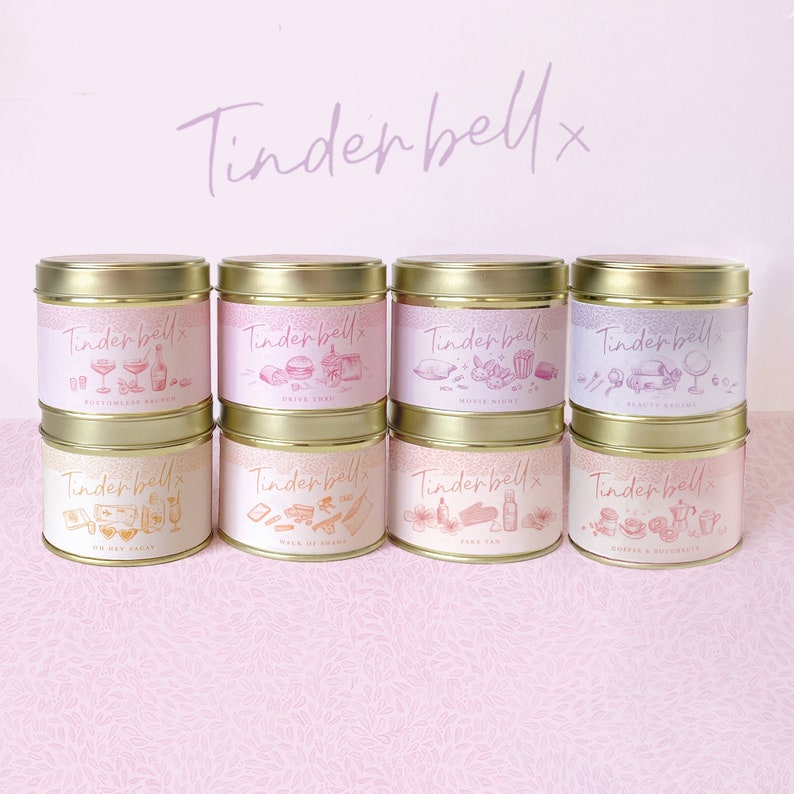 May include: Eight gold candle tins with pink and white labels. The labels feature illustrations of various activities and the text "Tinderbell" with a small "x" after it. The candle scents are: "Bottomless Brunch", "Drive Time", "Movie Night", "Pretty Rooms", "On The Hay Vacay", "Walk Up Shame", "Dark Tan", and "Coffee & Croissants".