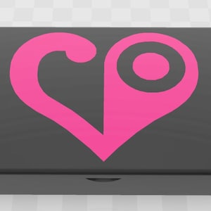 Può includere: Una scatola rettangolare nera con un design a forma di cuore rosa acceso sul coperchio. Il cuore ha una forma stilizzata unica con un elemento circolare. La scatola ha una finitura liscia e opaca.