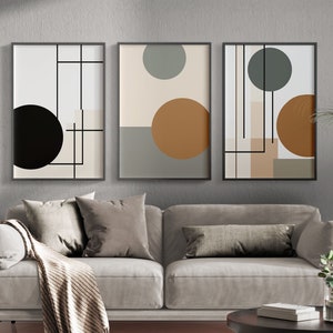 May include: Three framed abstract art prints. Each print features geometric shapes, including circles and lines, in neutral colors like black, beige, and brown. The artwork is displayed above a gray sofa with pillows and a blanket, creating a modern living room aesthetic.