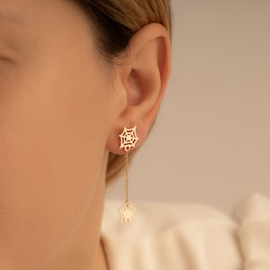 May include: Gold spider web dangle earrings with a small spider charm hanging from the bottom of the web.