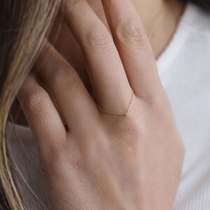 May include: A delicate gold chain ring worn on a finger.