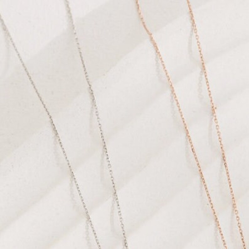 May include: Two delicate silver chains on a white background. One chain is silver and the other is rose gold.