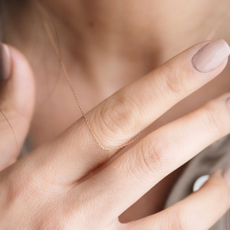 May include: A delicate rose gold chain necklace, shown draped over a hand.