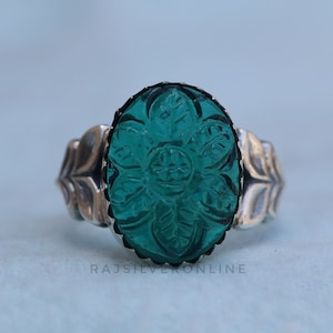 May include: A silver ring with a carved green glass stone in the shape of a flower.