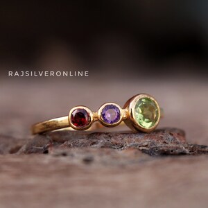 以下が含まれることがあります： 3つの宝石がついた金の指輪。赤いガーネット、紫のアメジスト、緑のペリドットです。