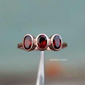 May include: A rose gold ring with three oval-shaped red gemstones.