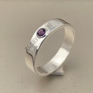 May include: A silver band ring with a small purple gemstone set in the center.