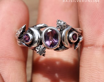 May include: A silver ring with three crescent moons and amethyst gemstones. The ring is decorated with small flower accents and a twisted vine design.