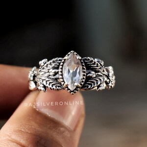 May include: A silver ring with a clear marquise-shaped gemstone surrounded by intricate floral designs.