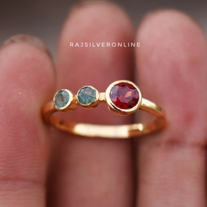 Peut inclure: Bague en or avec trois pierres précieuses. La pierre centrale est rouge, et les deux plus petites pierres de chaque côté sont vertes.